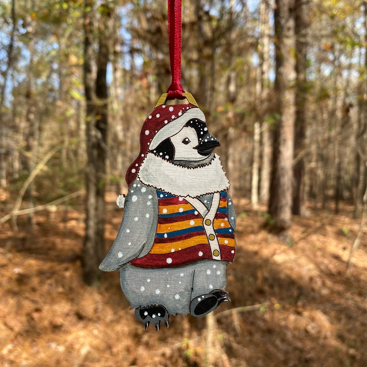A hand-painted ornament of a penguin wearing a red stocking hat and a striped sweater vest