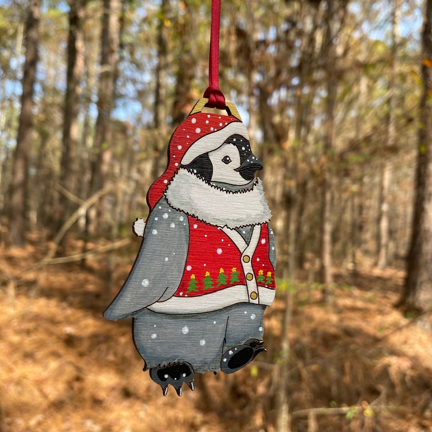 A hand-painted ornament of a penguin wearing a red stocking hat and a christmas tree sweater vest