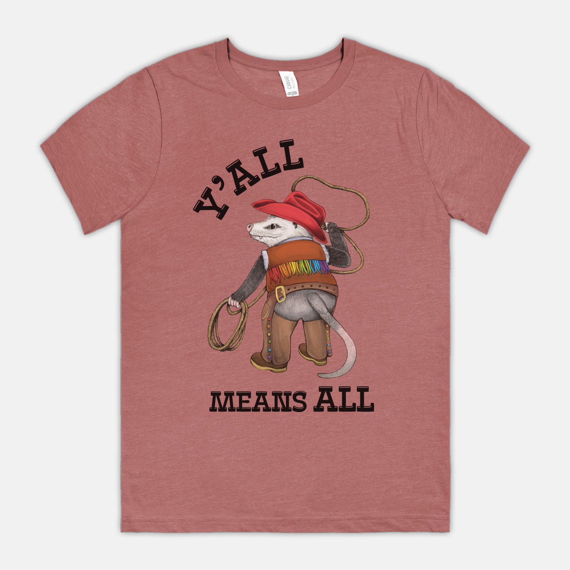 A mauve-colored shirt featuring a cowboy opossum and text reading “Y’all Means All”