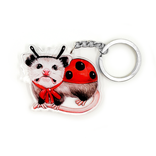 A keychain featuring an illustration of an opossum dressed as a ladybug