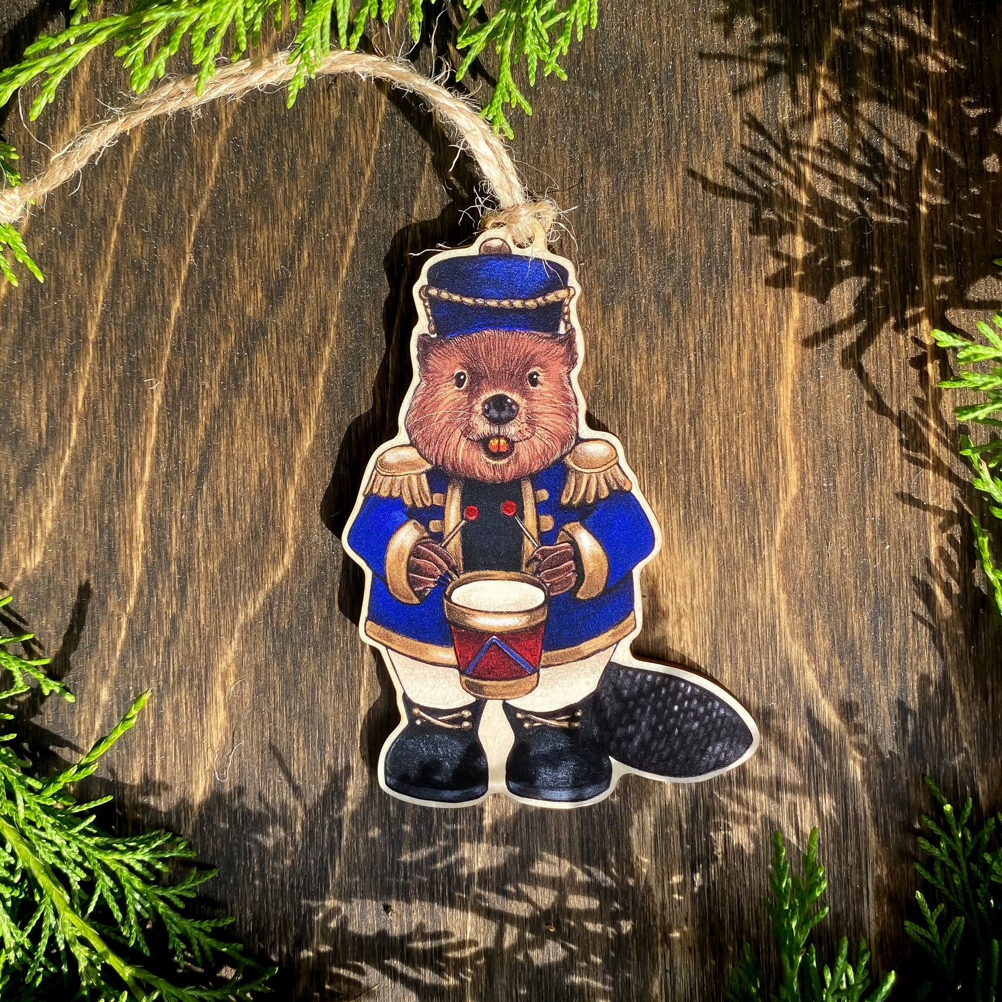 A wooden ornament strung with twine of a beaver in a blue nutcracker outfit.