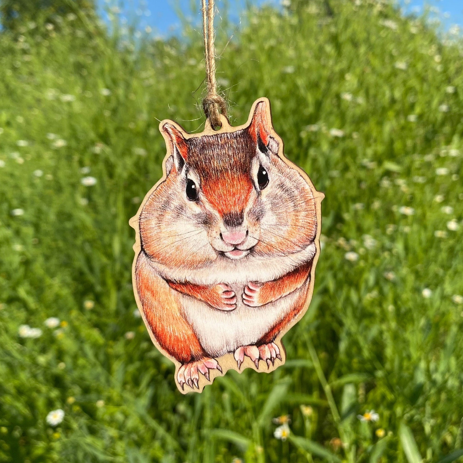 A wooden ornament strung with twine of an eastern chipmunk with full cheeks.