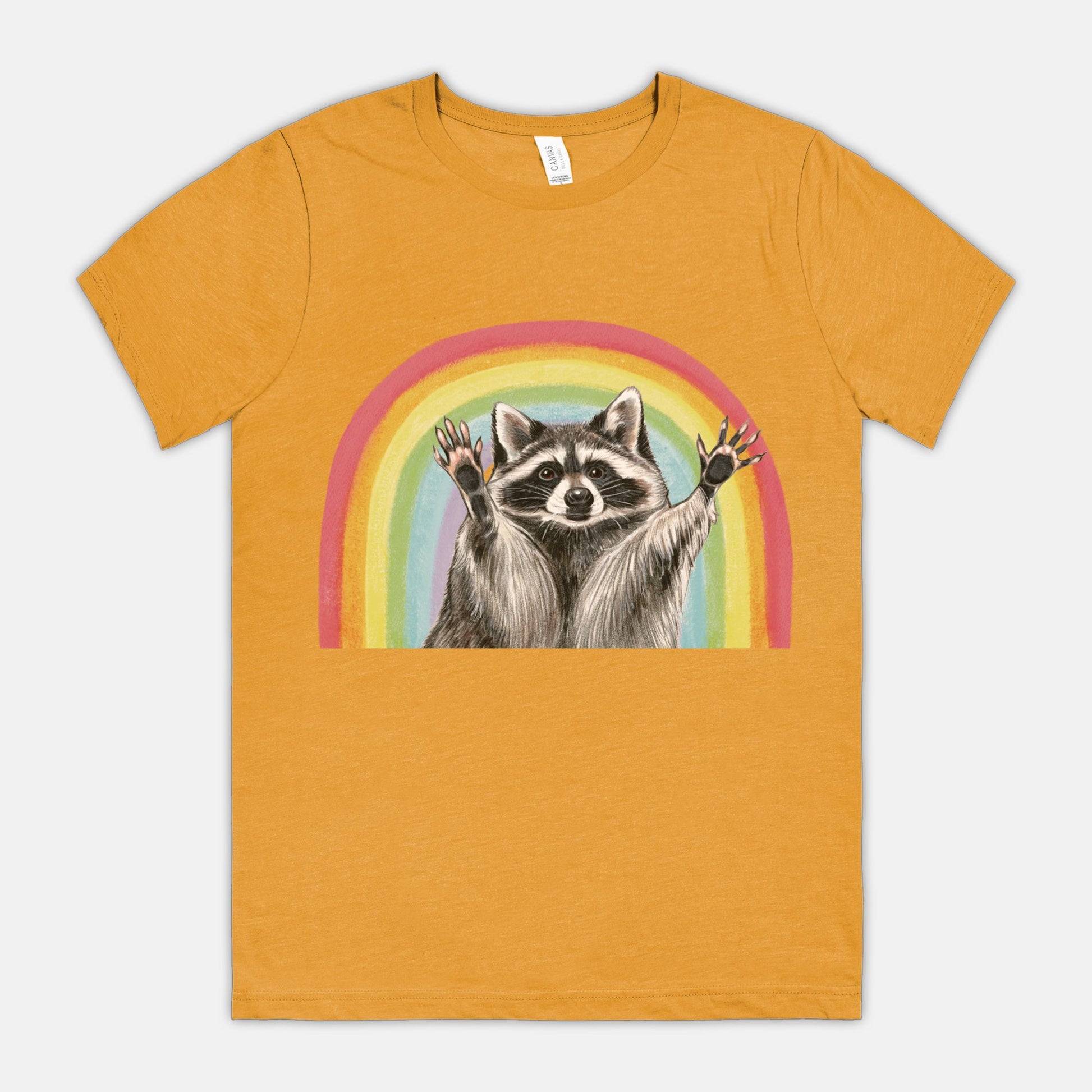 A yellow t-shirt featuring an illustration of a raccoon with raised hands in front of a rainbow.