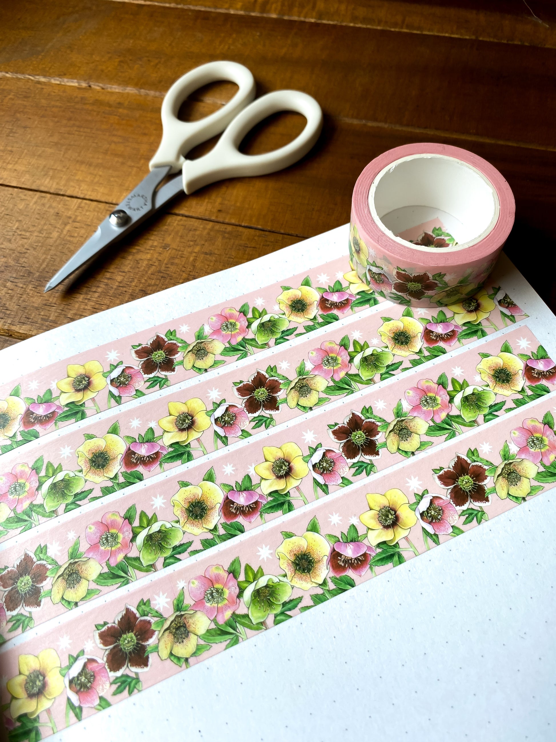 Washi tape with lenten roses/hellebores on a pink starry background swatched in a dot grid notebook.