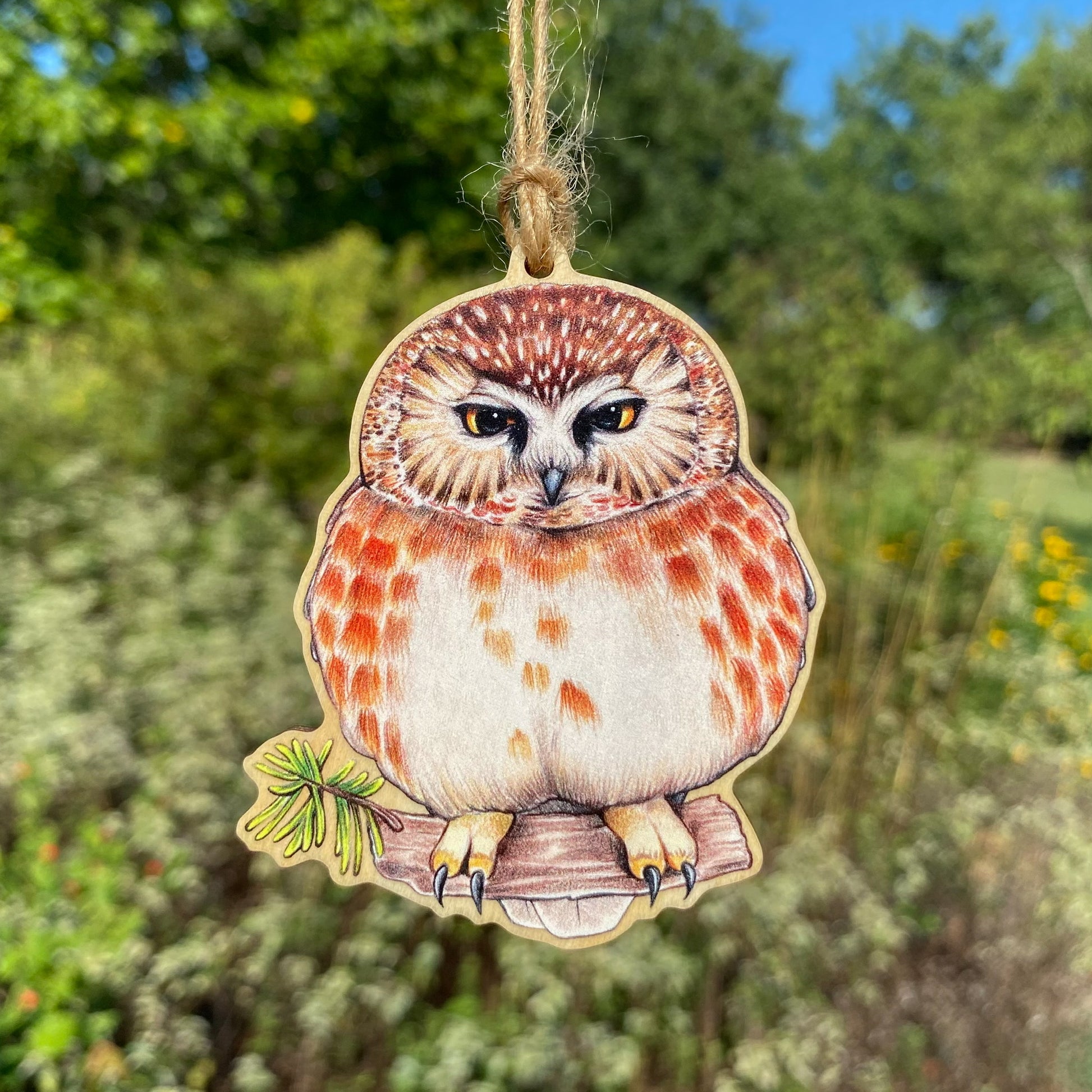 A wooden ornament strung with twine of a grumpy saw-whet owl.