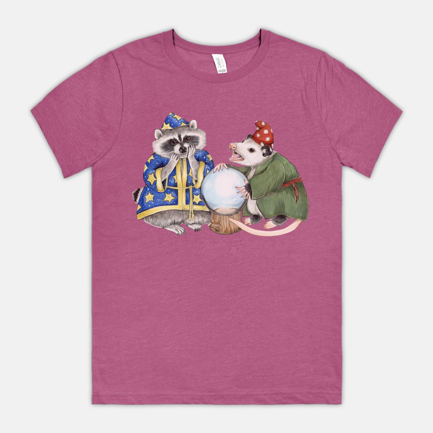 A magenta t-shirt featuring an illustration of a raccoon wizard and opossum fortune teller