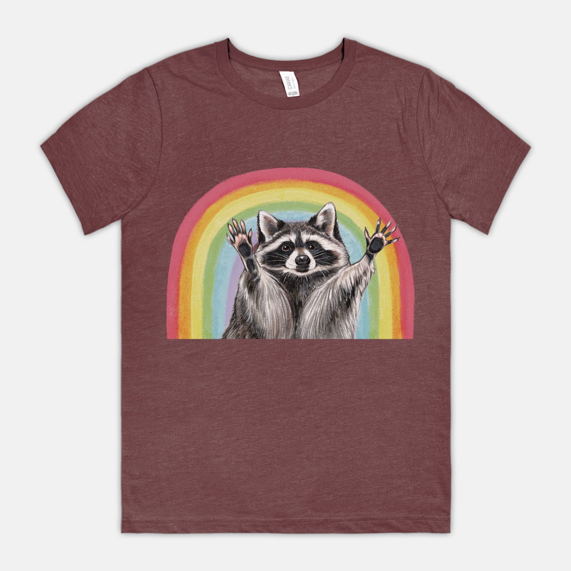 A rust-colored t-shirt featuring an illustration of a raccoon with raised hands in front of a rainbow.