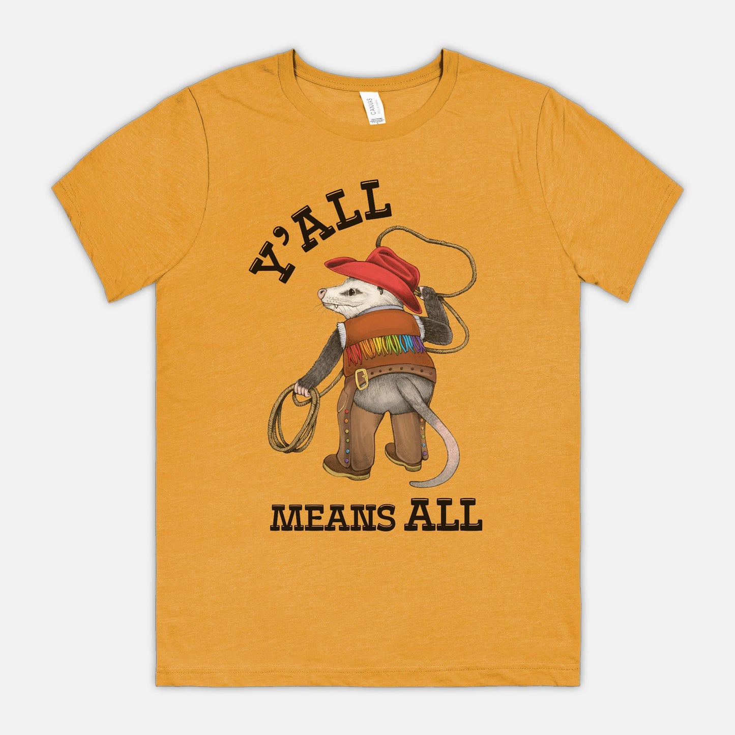 A mustard-colored shirt featuring a cowboy opossum and text reading “Y’all Means All”