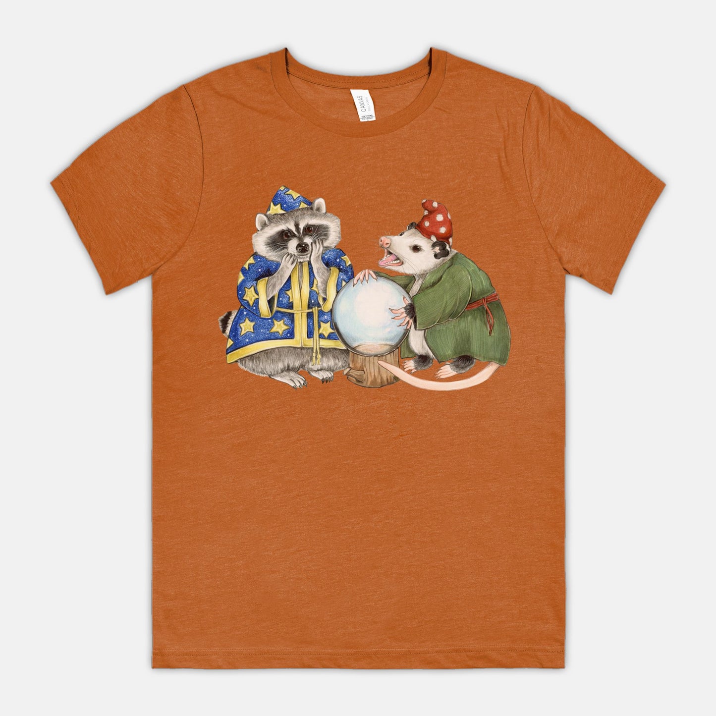 An orange t-shirt featuring an illustration of a raccoon wizard and opossum fortune teller