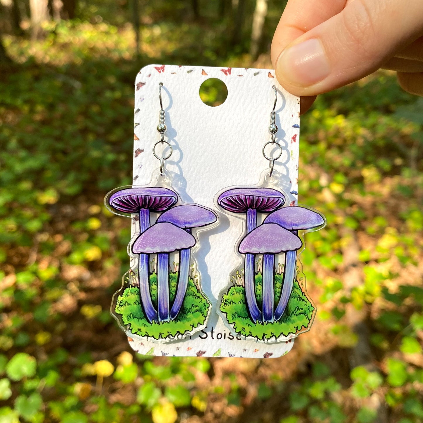 A hand holding a pair of acrylic earrings of amethyst decievers