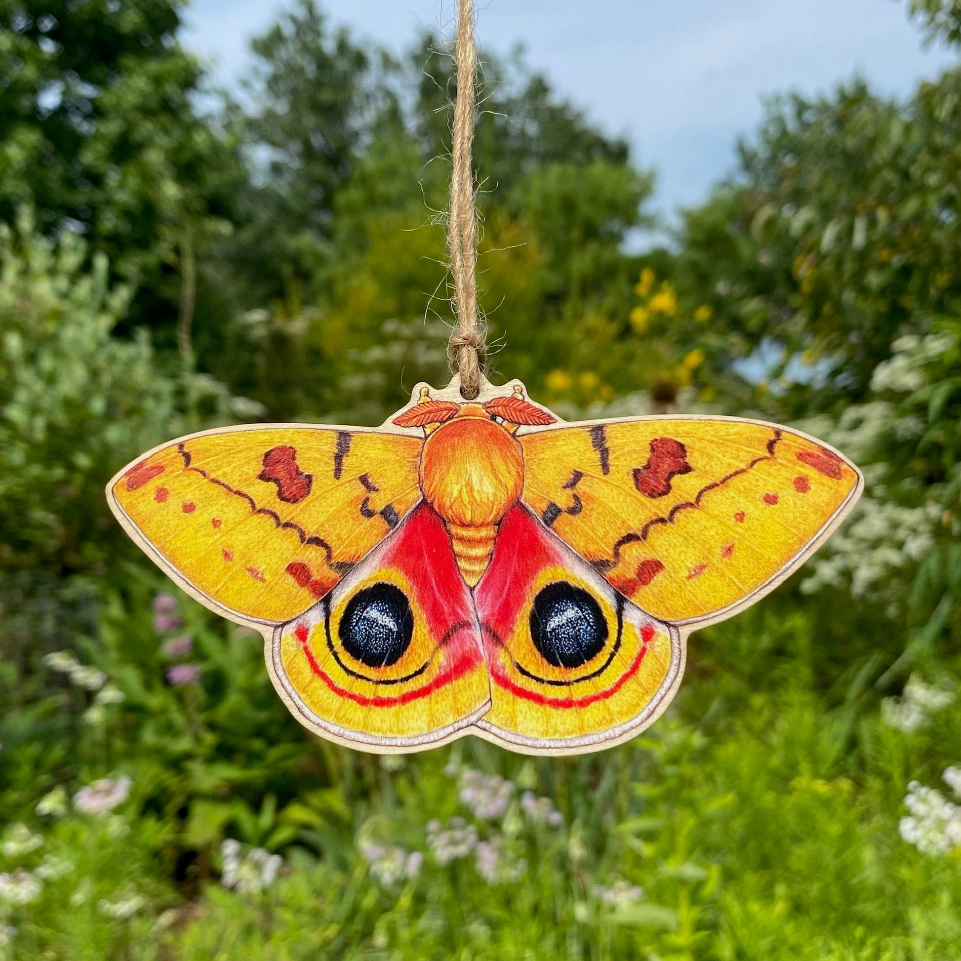 A wooden ornament strung with twine of a male io moth.