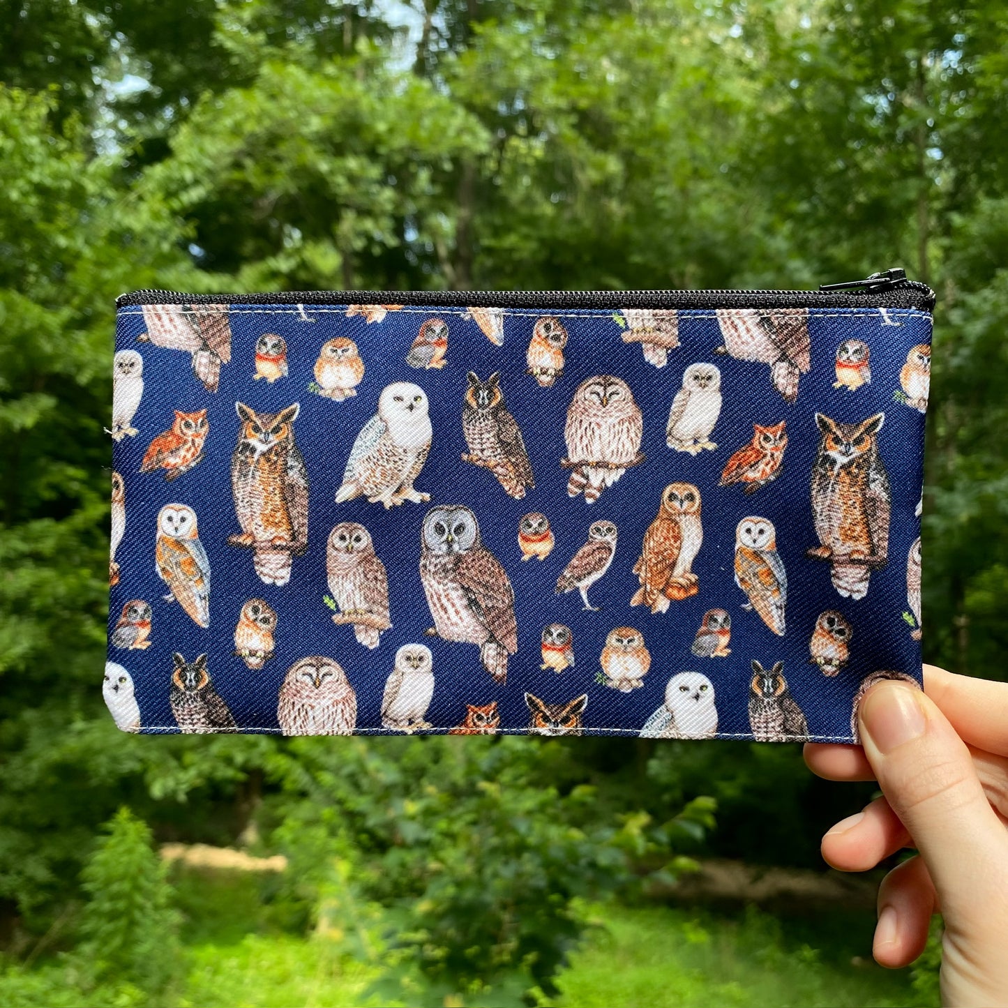 A hand holding a navy pouch with a pattern of owls on it.