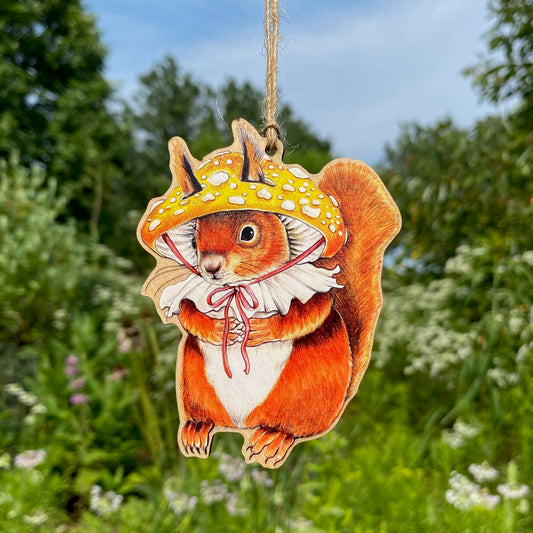 A wooden ornament strung with twine of a red squirrel wearing a yellow patches mushroom hat.