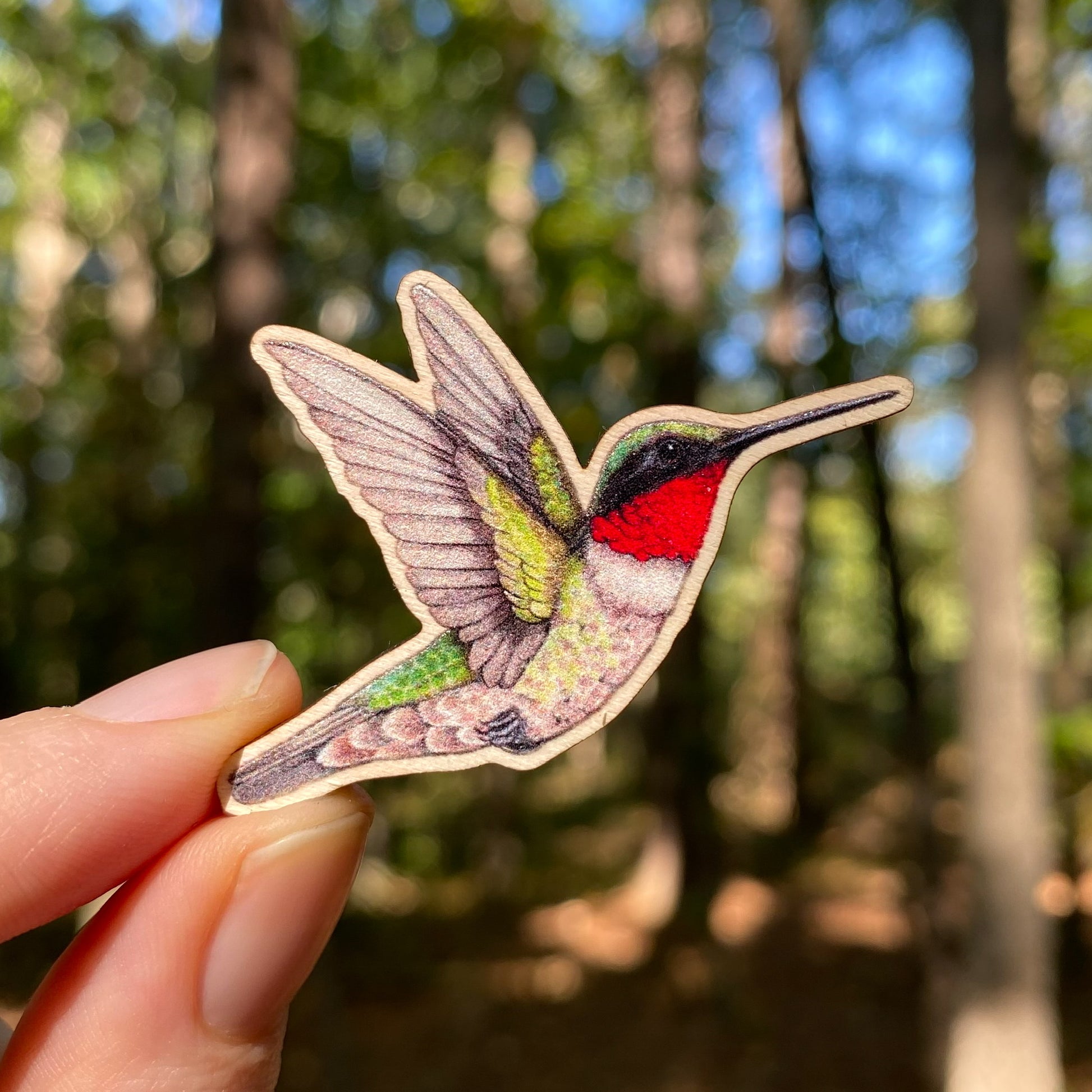 A wooden pin of a male ruby-throated hummingbird on a white background.