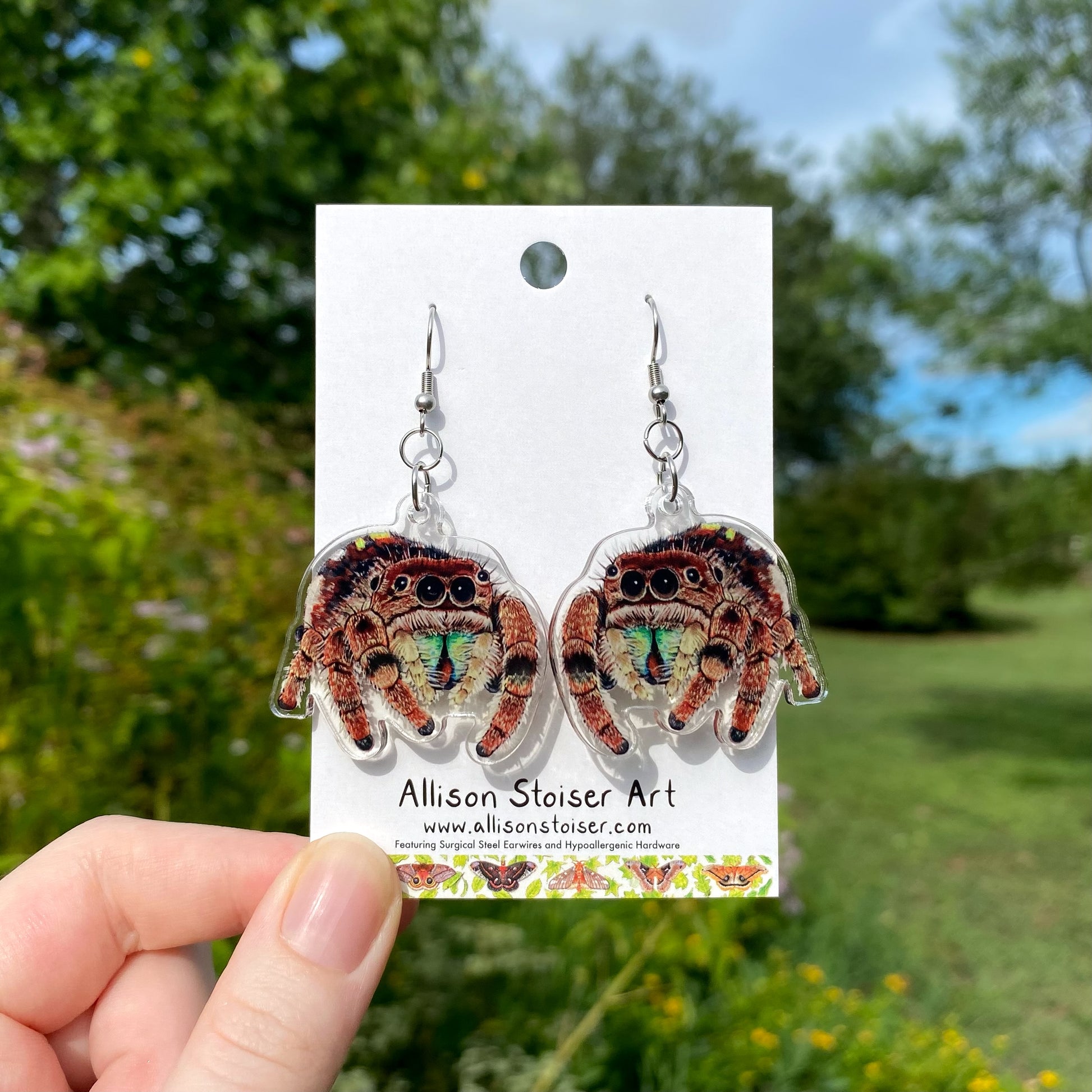 A hand holding a pair of acrylic jumping spider earrings.