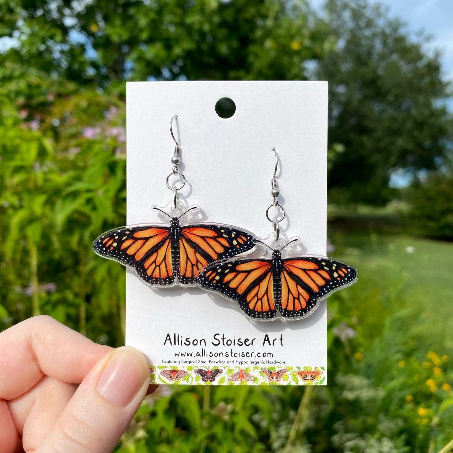 A hand holding a pair of acrylic monarch butterfly earrings.