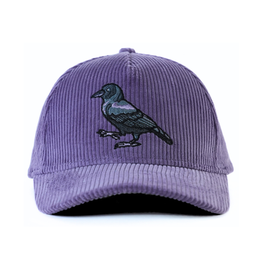 The front of a purple corduroy baseball cap with an embroidered crow on a white background.