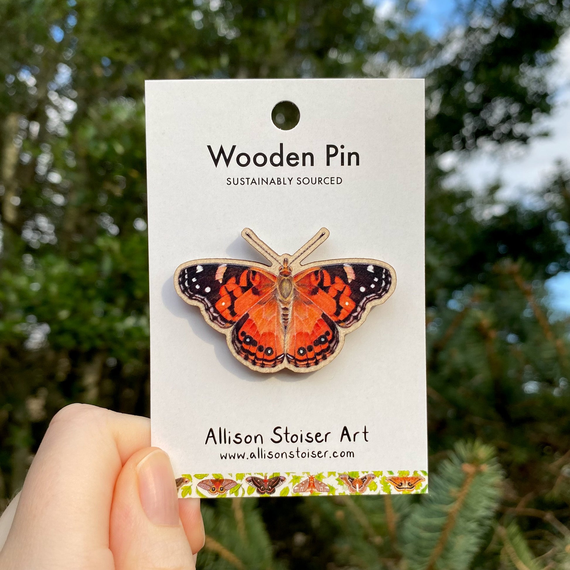A hand holding an American painted lady wooden pin.