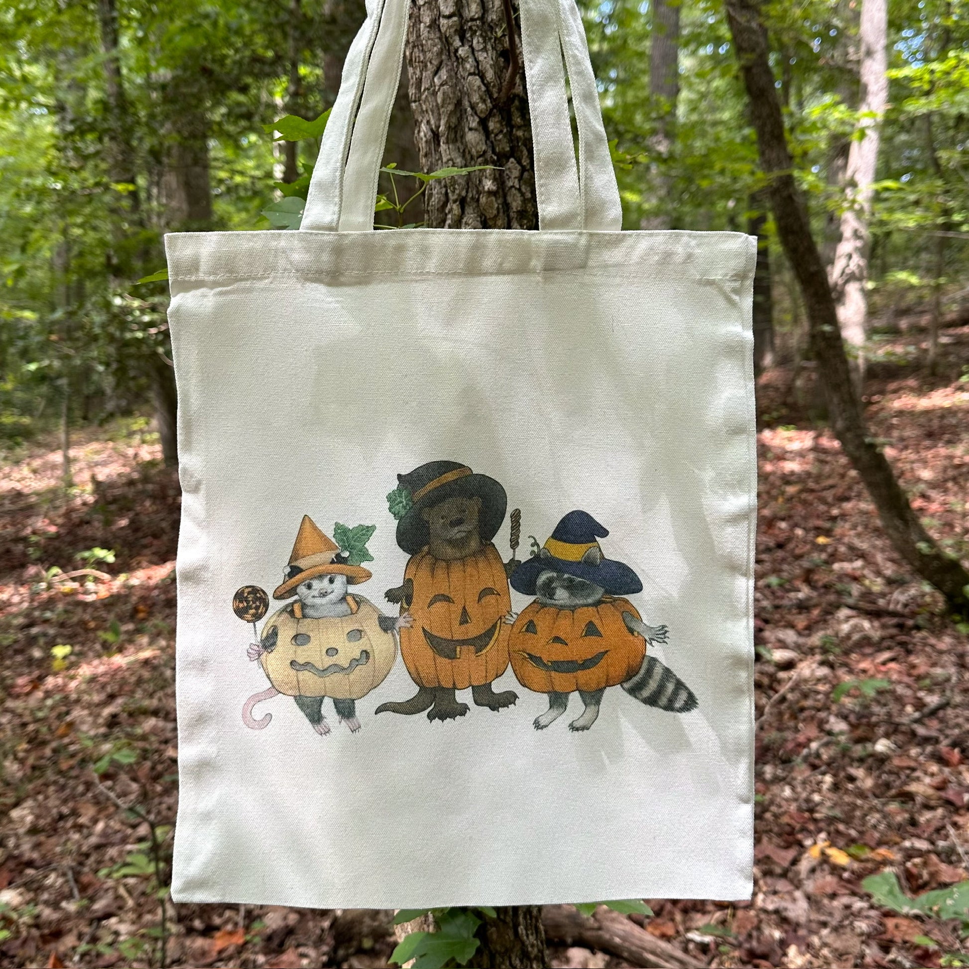 A tote bag featuring an illustration of a trio of animals dressed as pumpkins