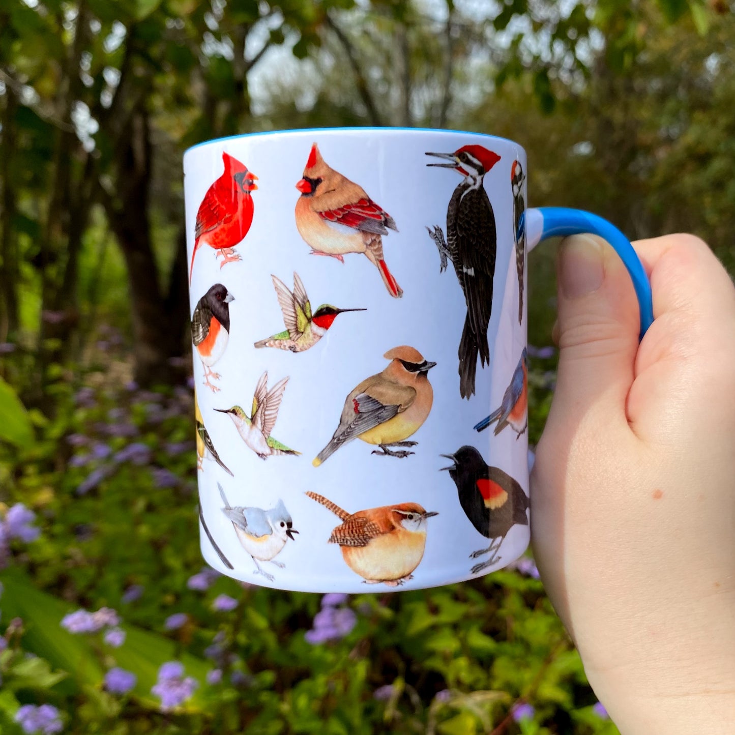 Mug with bird illustrations held in a hand against a natural background