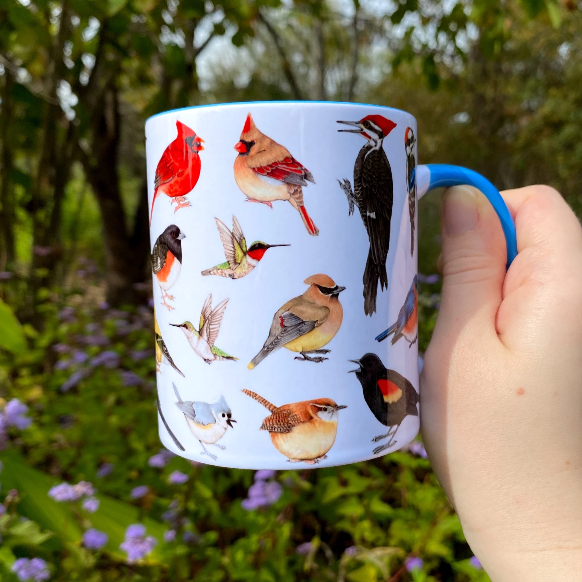 Mug with bird illustrations held in a hand against a natural background