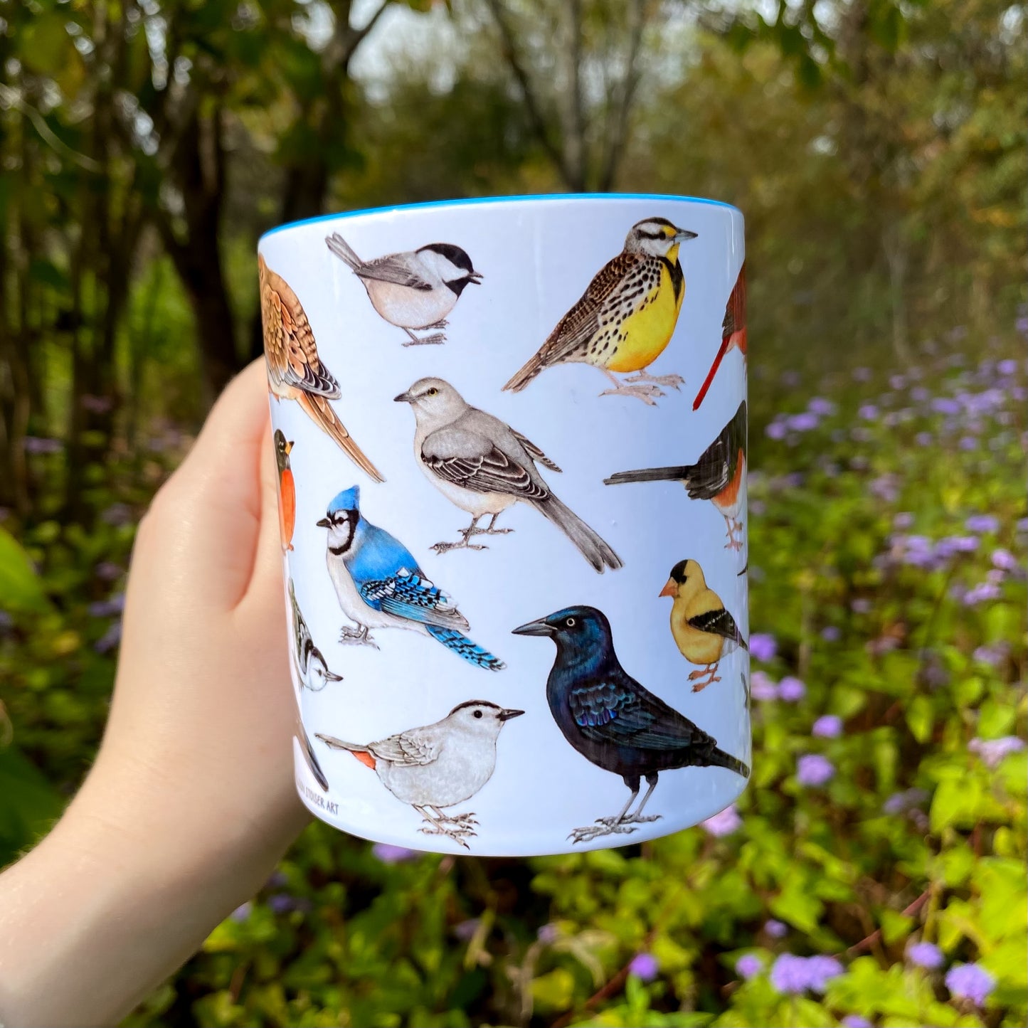 Cup with bird illustrations held in front of a natural background