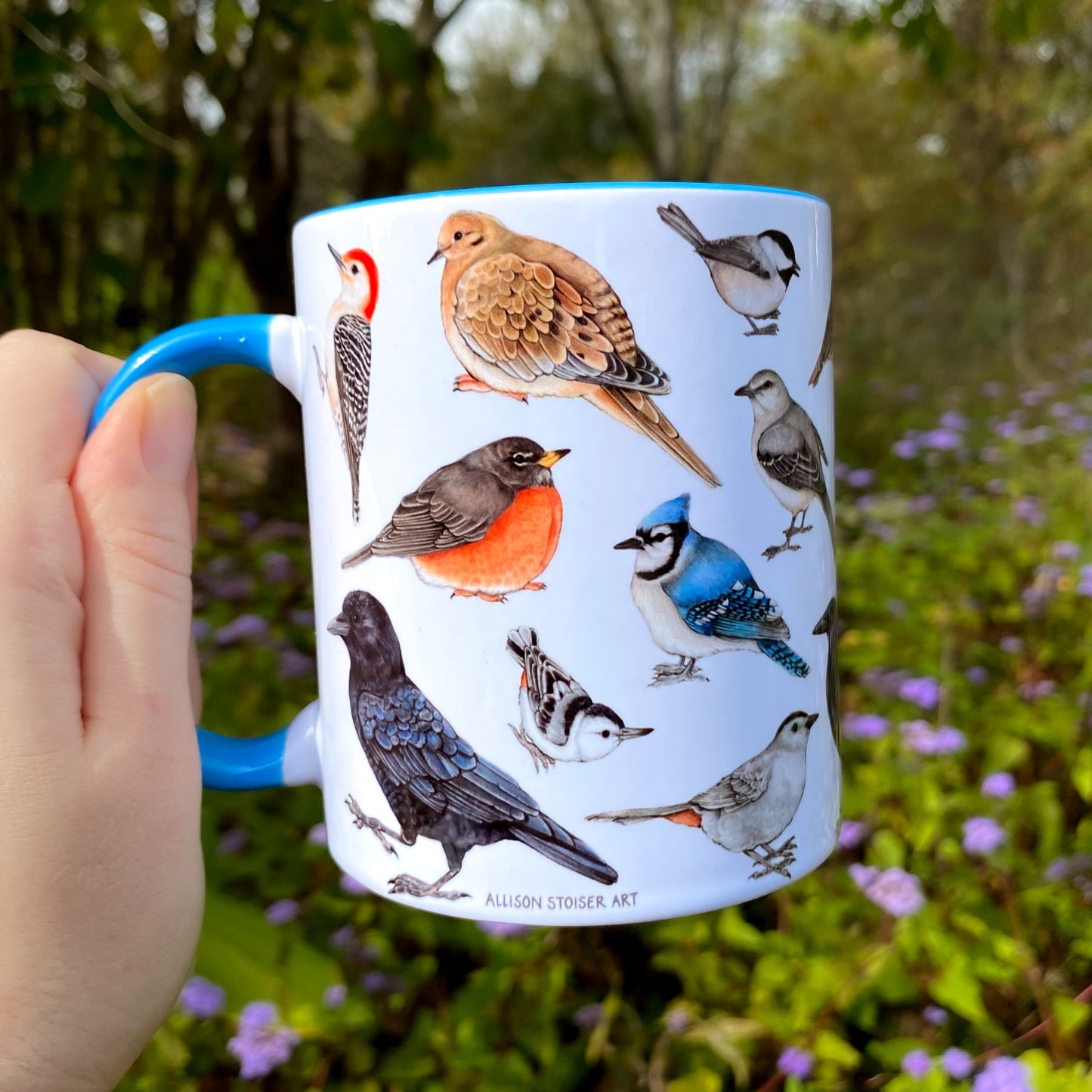 Mug with bird illustrations held by a hand in a natural setting