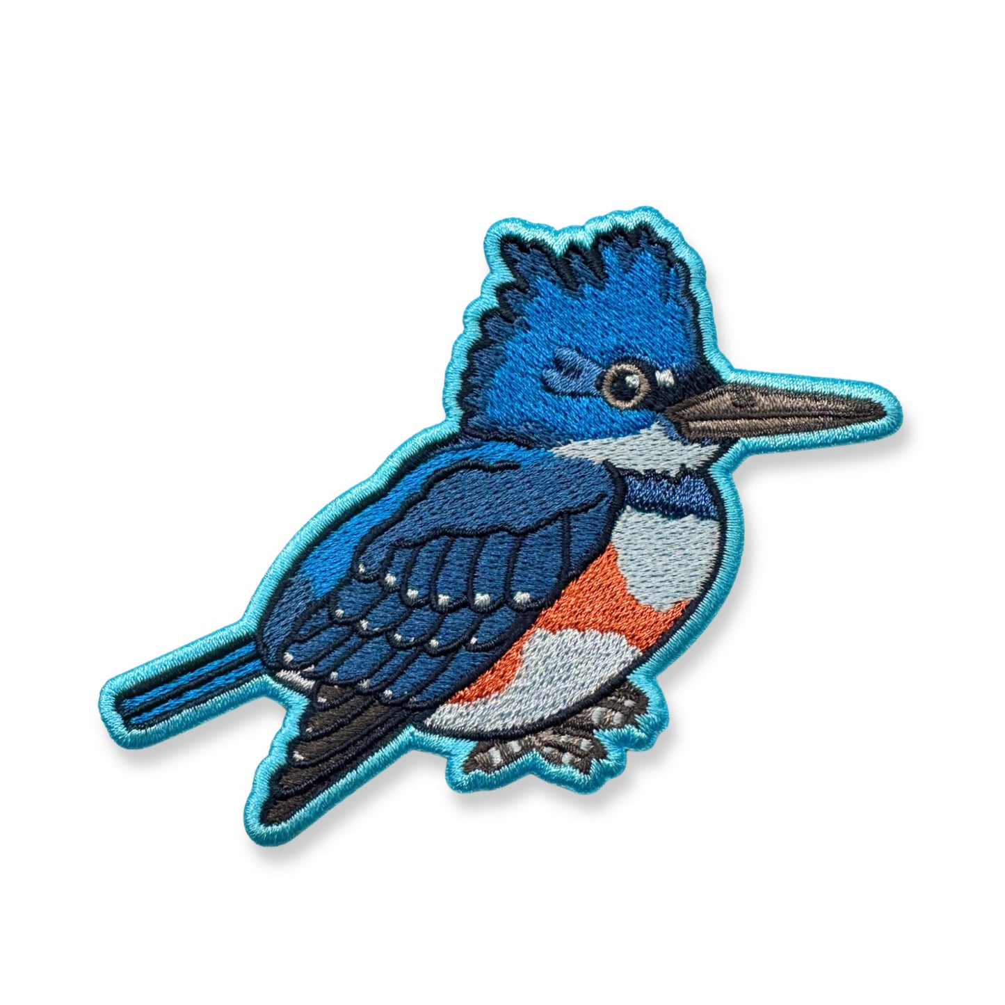An embroidered patch of a belted kingfisher shown on a plain white background.