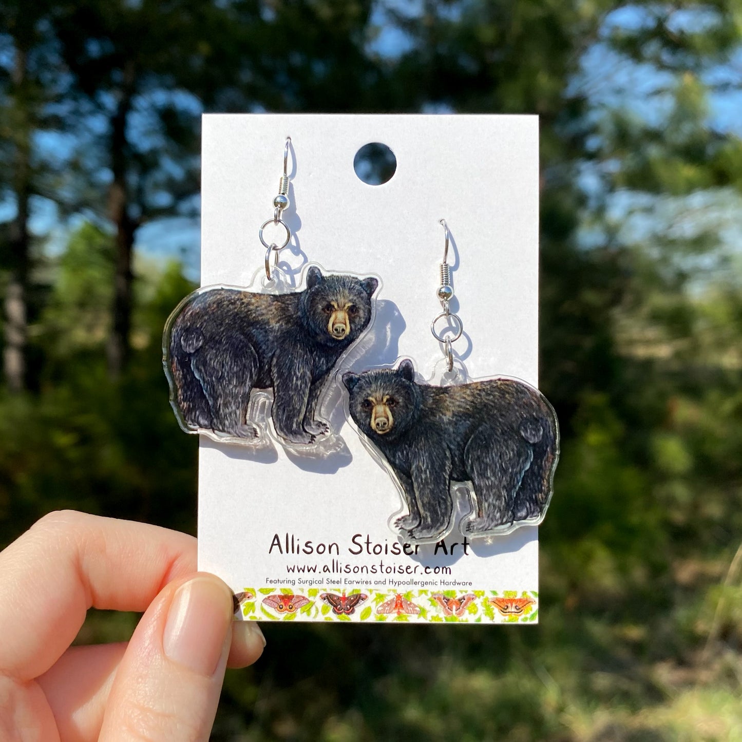 Acrylic black bear earrings on a card held by a hand with a natural background