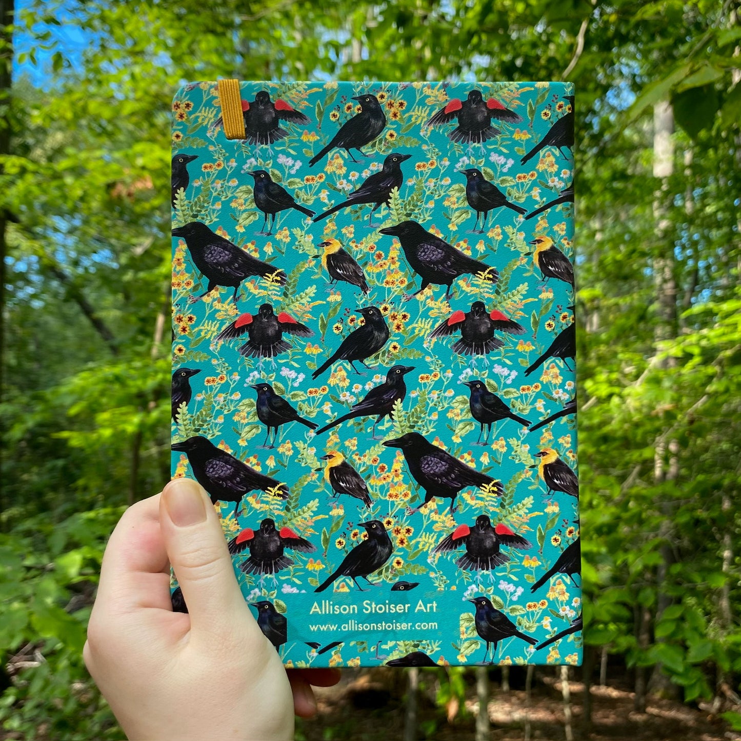 Notebook with blackbird and flower pattern held in front of a forest background