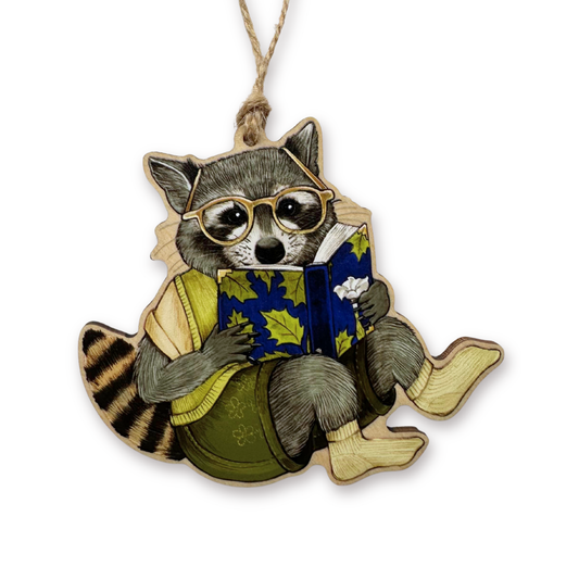 Decorative ornament of a raccoon wearing glasses and reading a book on a white background