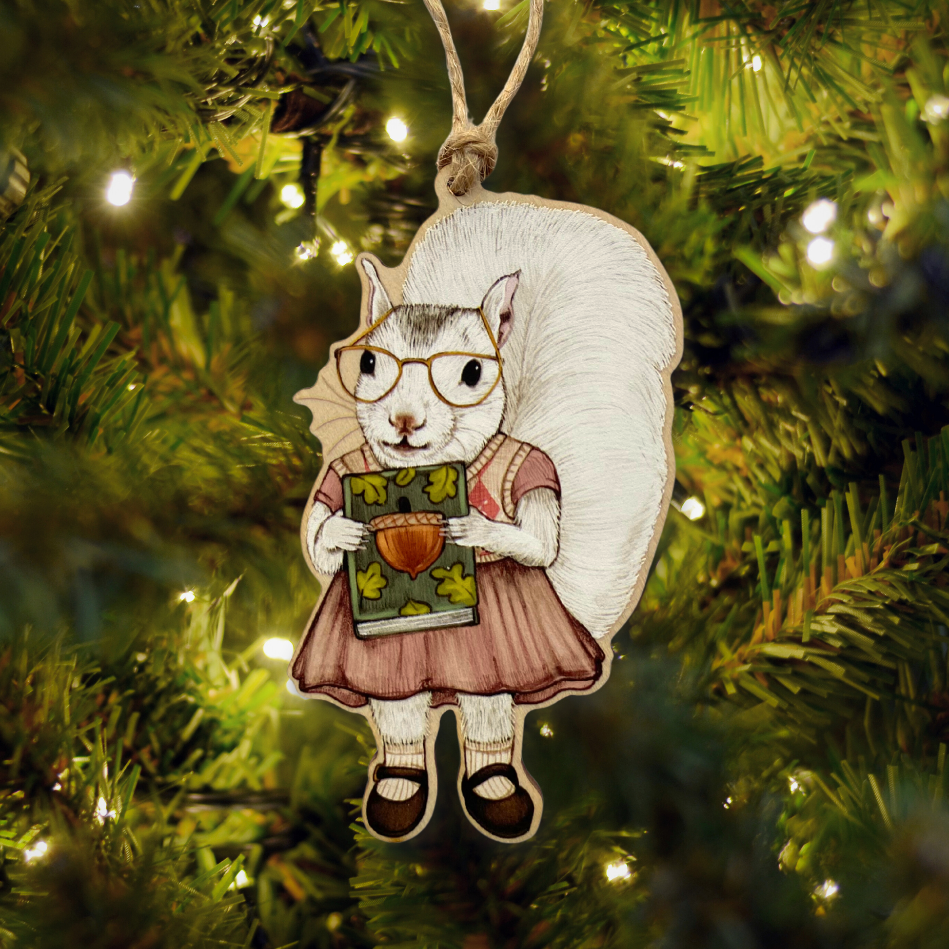 Decorative ornament of a squirrel holding a book, hanging on a Christmas tree.