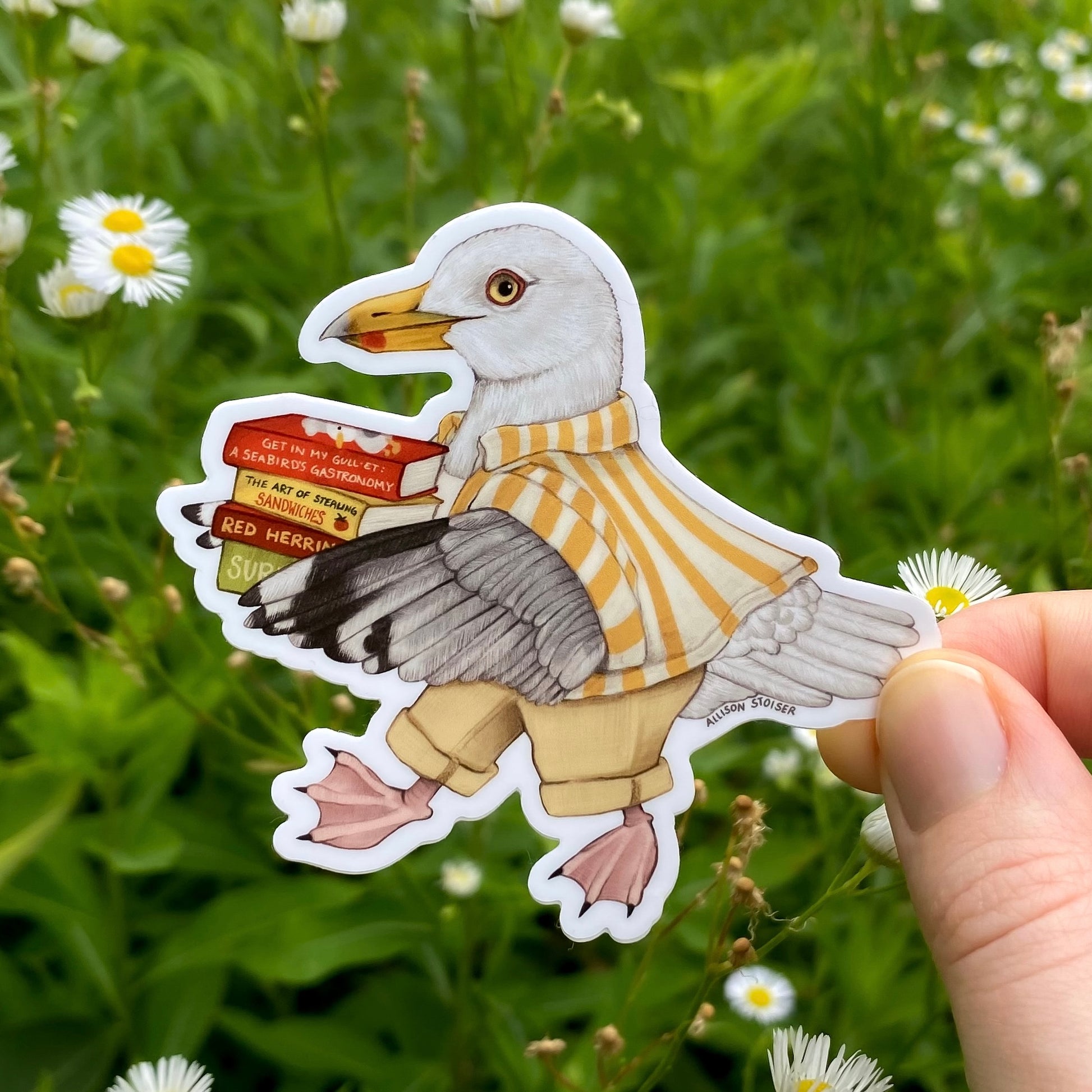 Sticker of a herring gull in a yellow and white striped shirt holding a stack of books held over a natural background with flowers.