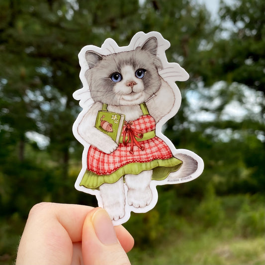 Sticker of a ragdoll cat in a dress held in front of a blurred natural background