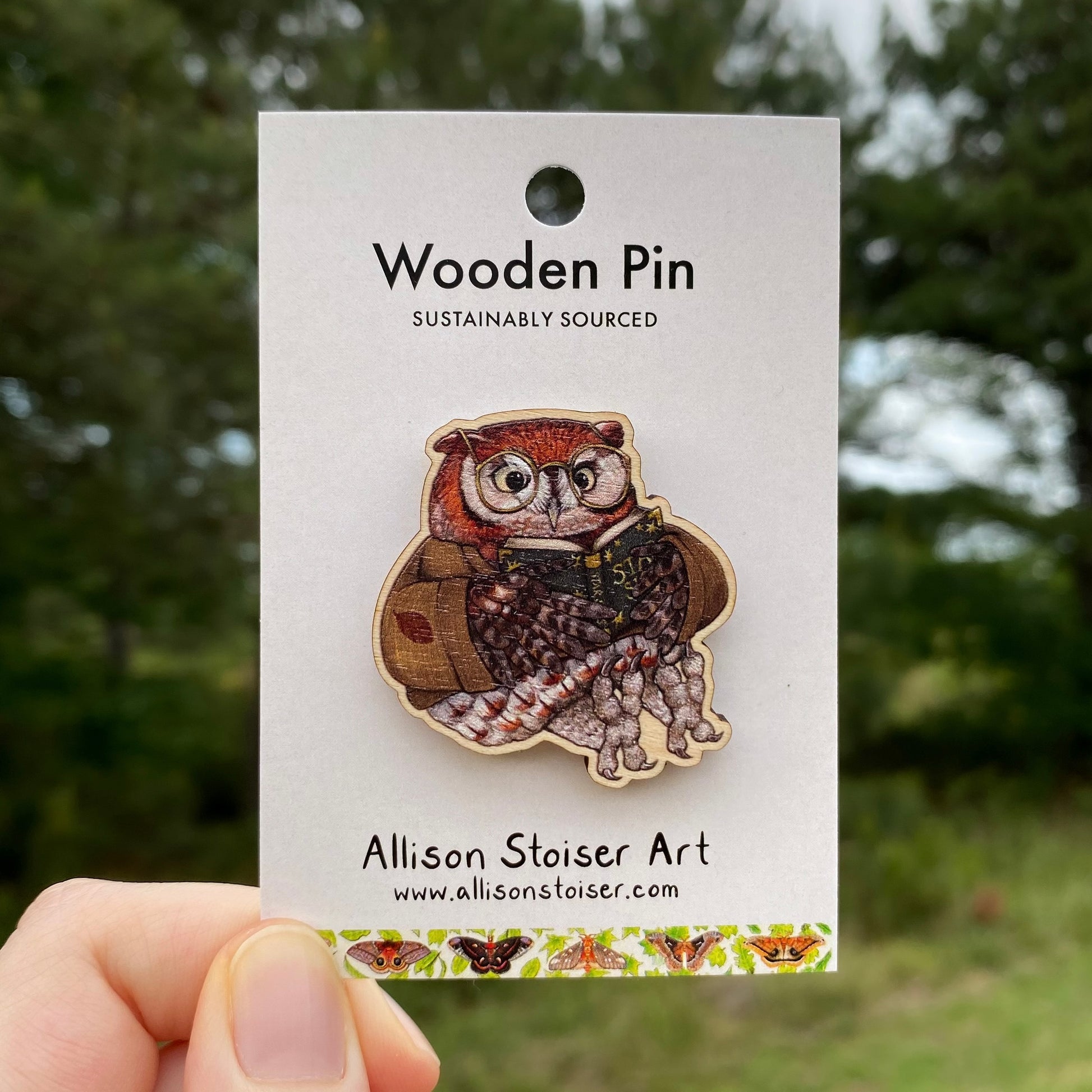 Wooden pin of an owl reading a book on a card labeled 'Allison Stoiser Art' against a blurred natural background.