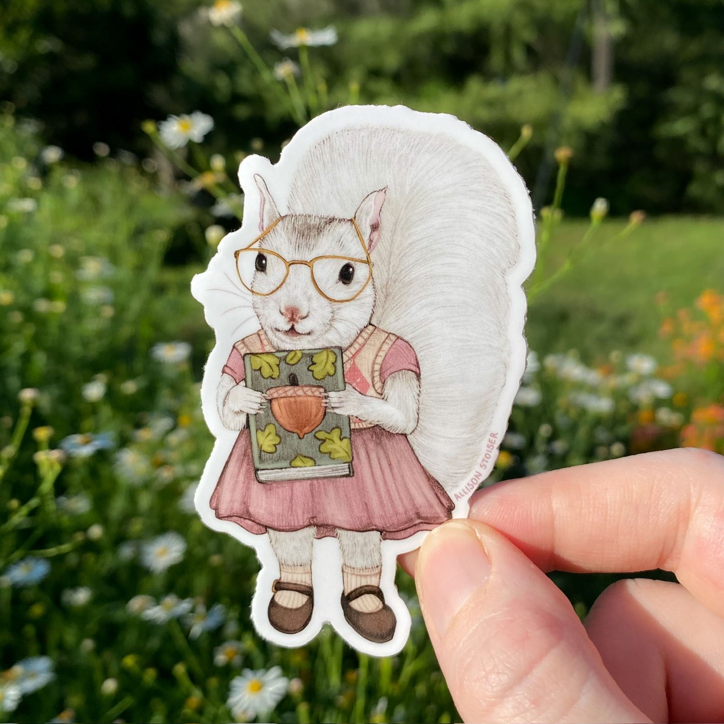Sticker of a squirrel in glasses and a dress held in front of a natural background with flowers and greenery.