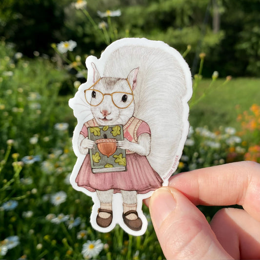 Sticker of a squirrel in glasses and a dress held in front of a natural background with flowers and greenery.