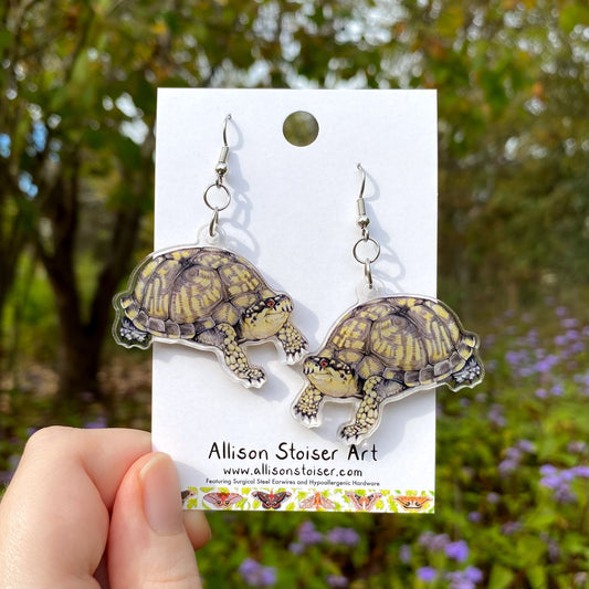 Box turtle earrings on a card held by a hand with a natural background