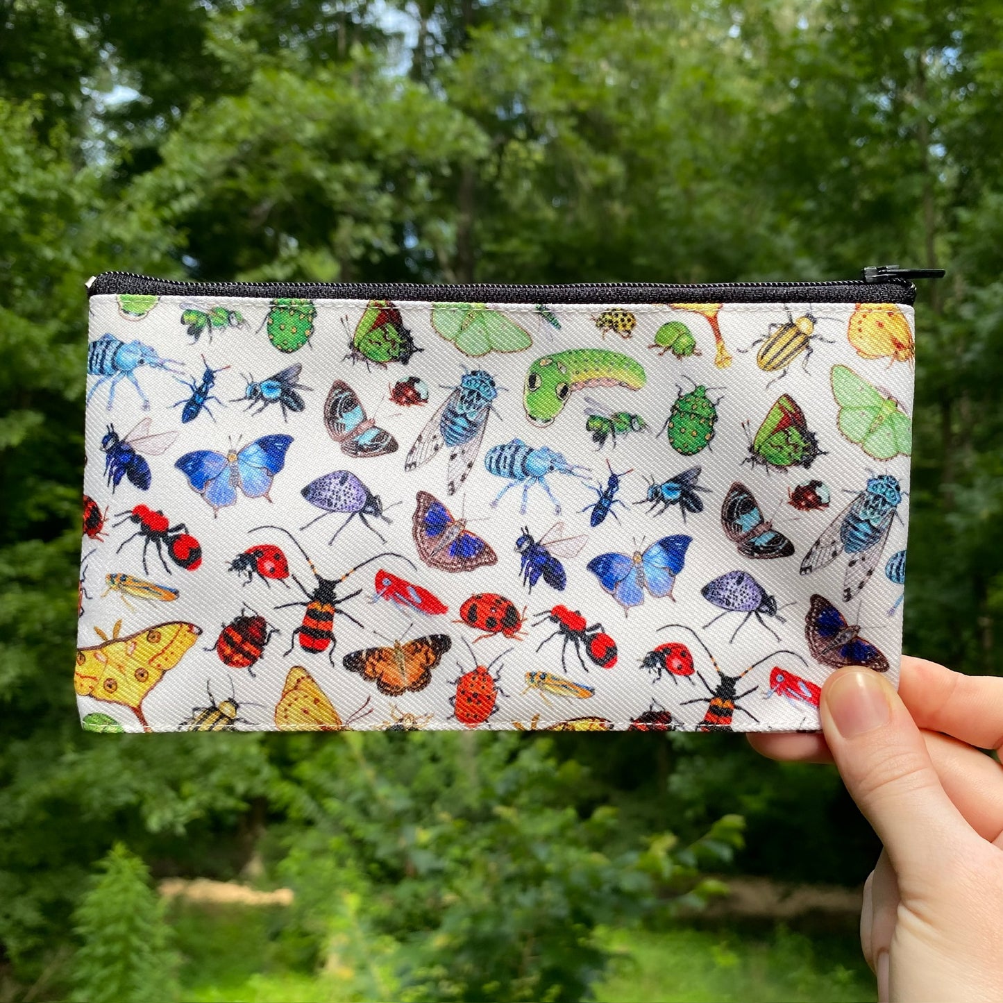 A hand holding a white pouch with rainbow of insects printed on it.