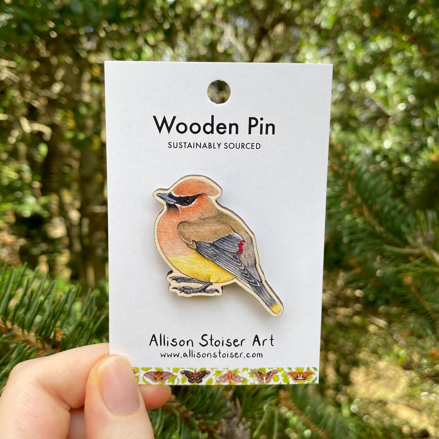 A hand holding a wooden pin of a cedar waxwing bird