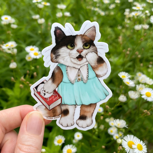 Sticker of a cat in a dress holding a book held in front of a field of daisies