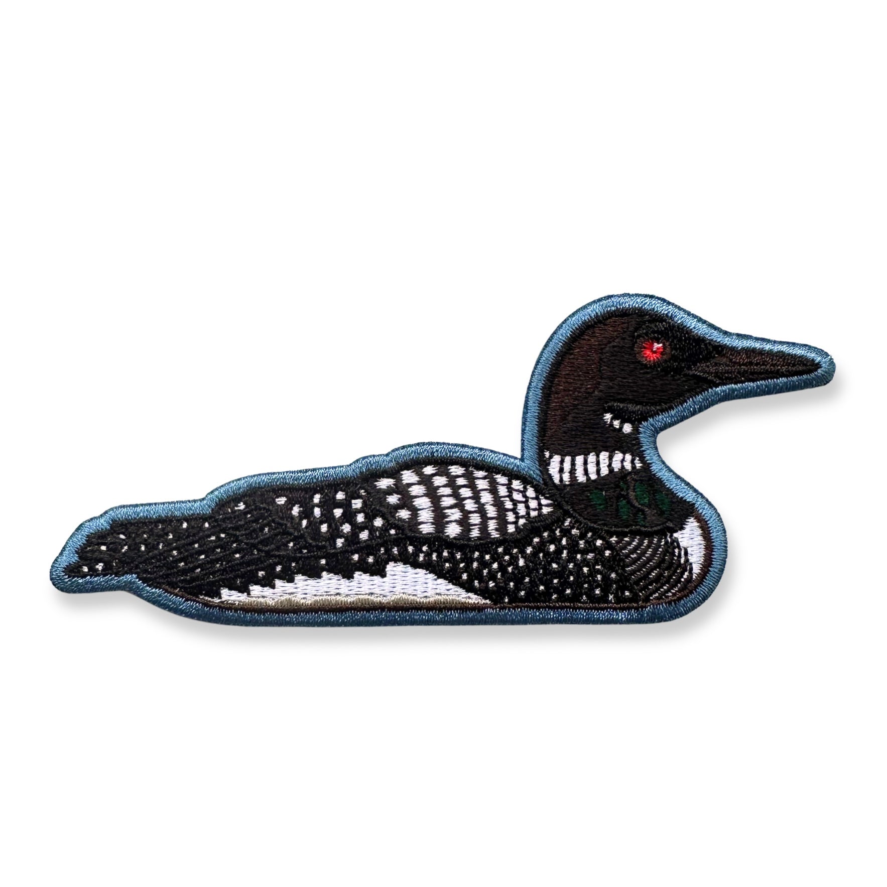 An embroidered patch of a loon in side profile, featuring a black body with white speckled markings, a dark green neck patch, and a small red eye, all outlined with blue-gray stitching on a white background.