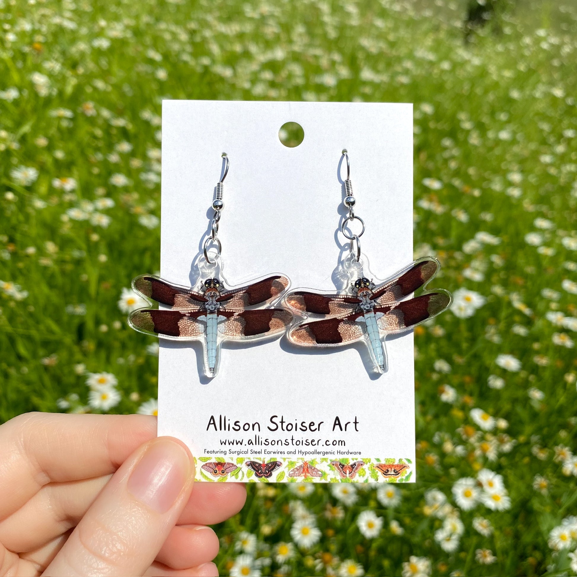 A hand holding a pair of clear acrylic earrings of dragonflies.