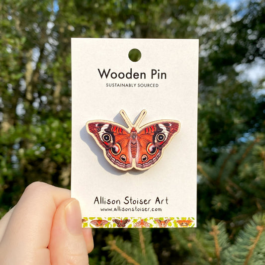 A hand holding a wooden pin of a common buckeye butterfly