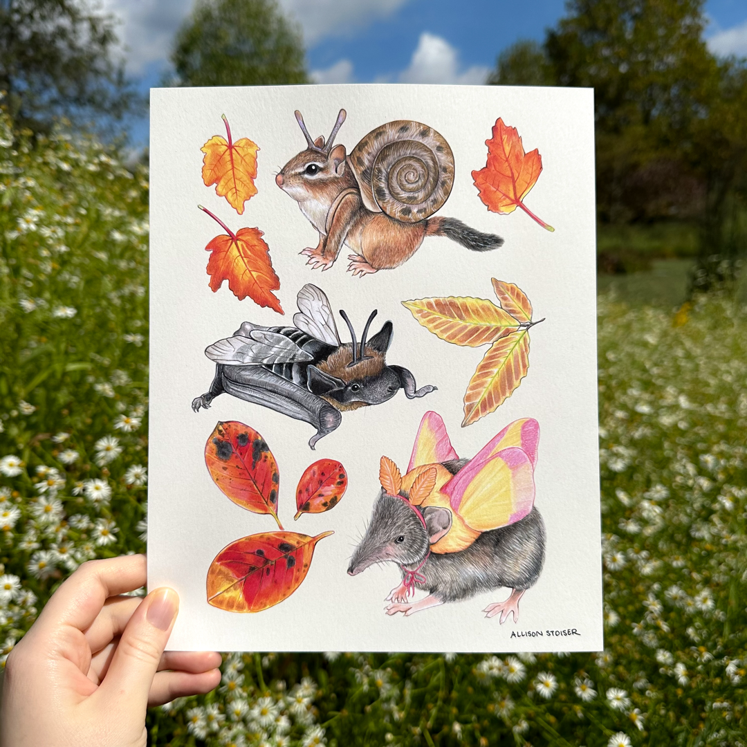 A hand holding a print featuring a spread a costumed chipmunk, bat, and shrew and fall foliage. 