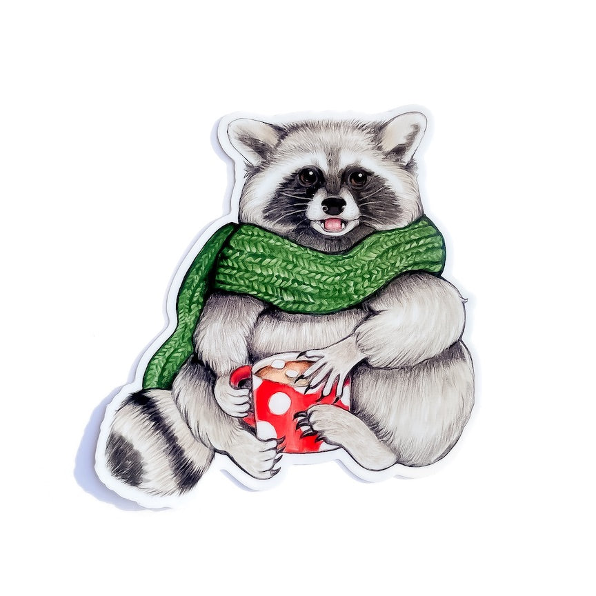 A weatherproof vinyl sticker of a cozy raccoon holding a mug of hot chocolate with marshmallows on a white background.