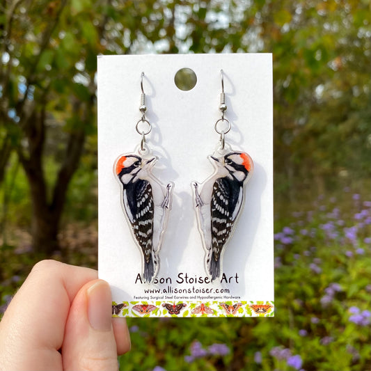 Downy woodpecker earrings on a card held by a hand with a natural background