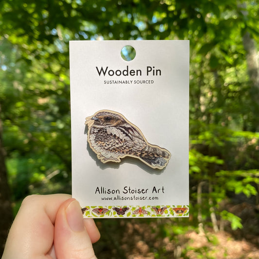 A wooden pin of a whip-poor-will on packaging that reads Wooden Pin, Sustainably Sourced.