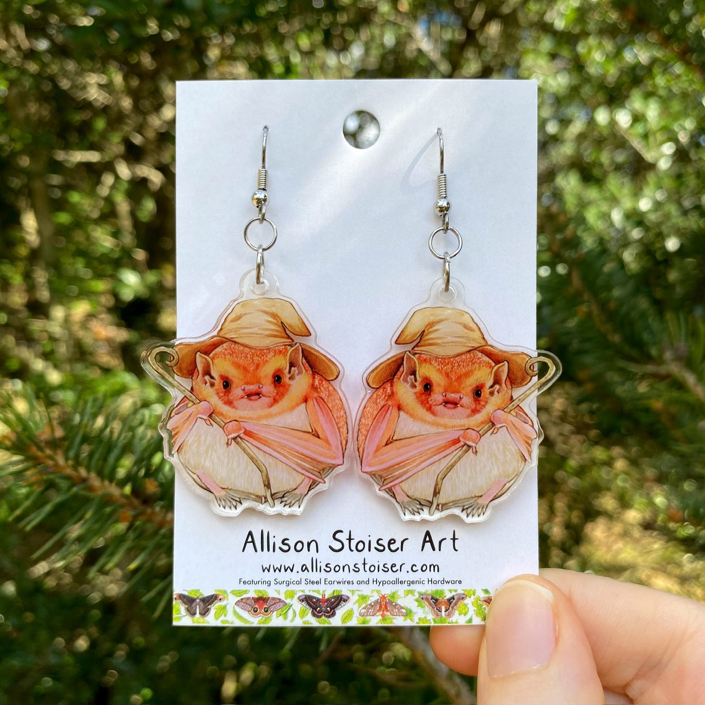 A hand holding a pair of eastern red bat wizard acrylic earrings