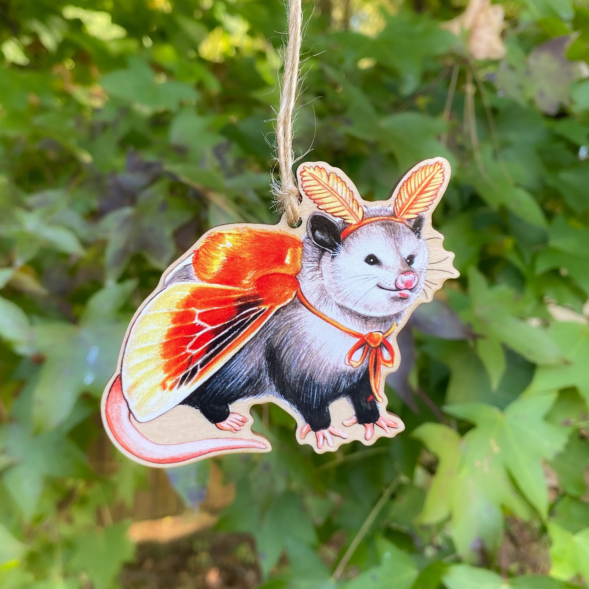 A wooden ornament strung with twine of an opossum in an orange flannel moth costume.